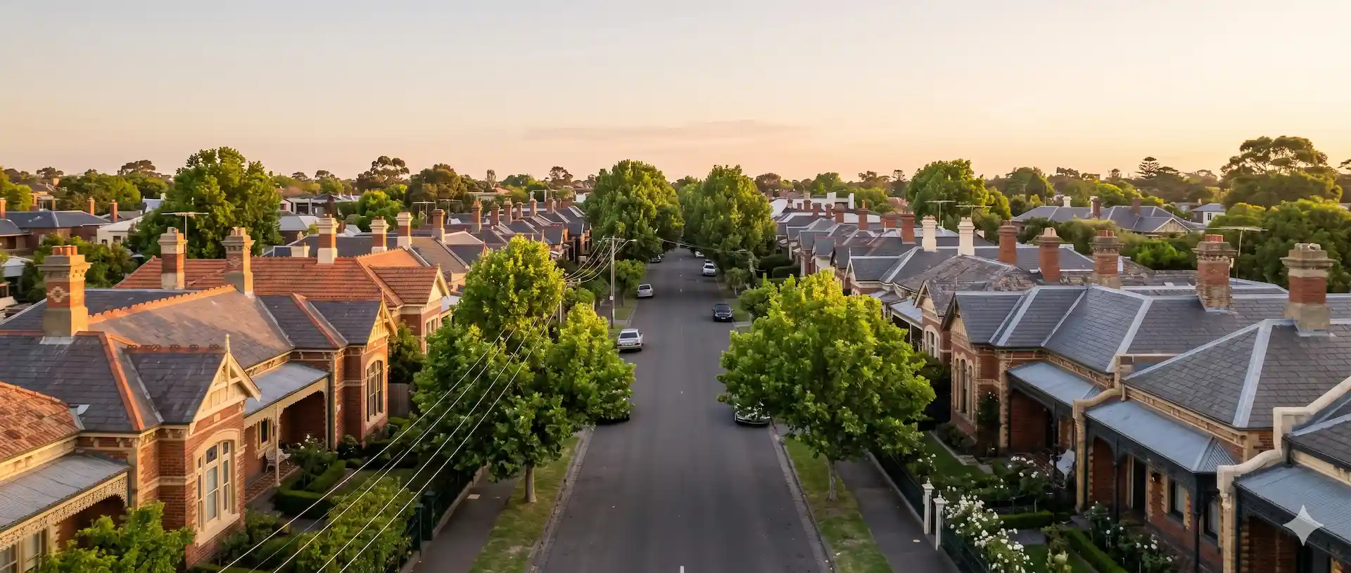 Aerial view of a leafy inner-east Melbourne street, lined with red-brick Victorian and Edwardian rooflines at golden hour.